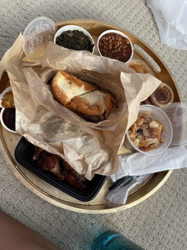 Meal from City Barbecue: brisket sandwich, greens, baked beans, smoked wings, and peach cobbler on a gold tray.