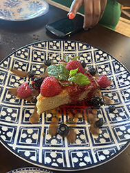 A slice of cake sits on a plate covered in mint, berries, and caramel sauce. The kind of cake friends share.