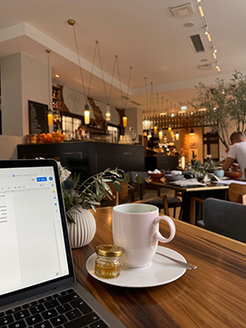 Table in a coffee shop with a cup, laptop, and succulent on top.